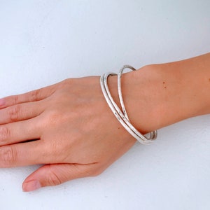May include: A set of four silver bangles stacked on a wrist. The bangles are smooth and have a slightly hammered texture.
