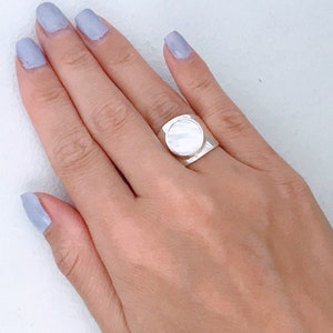 May include: A silver ring with a large, round, white mother-of-pearl stone set in the center.