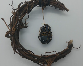 May include: A black gemstone wrapped in copper wire hangs from a crescent moon-shaped wreath made of brown twigs.