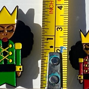 May include: Two black and gold nutcracker figurines with yellow crowns. The nutcracker on the left is wearing a green jacket and the nutcracker on the right is wearing a red jacket. Both nutcrackers have black hair and brown eyes.
