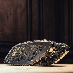 May include: A detailed, intricate, metal model of a tank with gold-coloured gears and tracks. The model is made of metal and has a black finish.