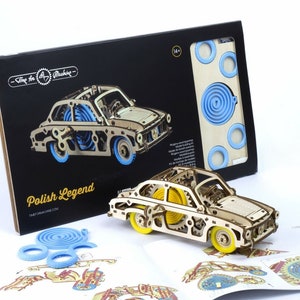 May include: A wooden model car kit of a Polish Legend car. The kit includes a detailed wooden model, instructions, and blue rubber bands. The box features a black background with the words "Time for a Workshop" and "Polish Legend".