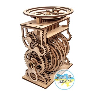 May include: Wooden 3D puzzle featuring intricate gears and a circular platform on top. The puzzle is crafted from natural wood and has a light brown colour. The puzzle is labelled "Made in Ukraine".