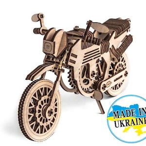 May include: A wooden model kit of a motorcycle, with intricate details and a working mechanism. The model is made of natural wood and features a brown and black colour scheme. The motorcycle is on a white background with a blue and yellow sticker that says "Made in Ukraine".