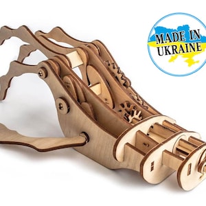 May include: A wooden model of a robotic hand with gears and moving parts. The hand is made of light brown wood and has a claw-like grip. The model is labelled "Made in Ukraine".