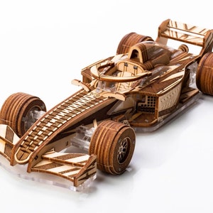 May include: A wooden model of a Formula One race car with a zebra-like pattern. The car has a clear plastic windshield and detailed wooden wheels.