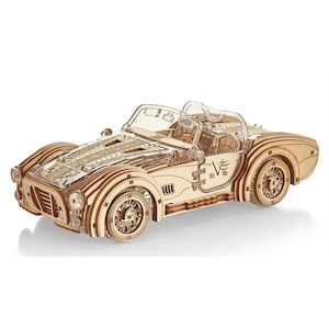 May include: A wooden model kit of a classic sports car, featuring a detailed design with a transparent windscreen and a V8 logo on the side. The model is made of natural wood and is ready to be assembled.