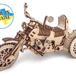 May include: A detailed wooden model of a three-wheeled motorcycle. The model is constructed from light brown wood and showcases intricate features such as the engine, seat, and wheels. The image includes a blue and yellow circle with the text "MADE IN UKRAINE".