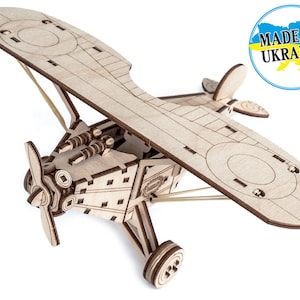 May include: Wooden model aircraft kit of a vintage biplane with a propeller, wheels, and a rubber band for propulsion. The kit is made in Ukraine and is ready to be assembled.