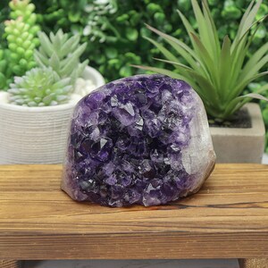 May include: A large, polished amethyst geode with deep purple crystalline structures. The geode is displayed on a wooden surface, showcasing its natural beauty and intricate details. The geode is a striking decorative item.