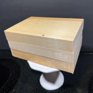May include: A stack of three rectangular light-colored wooden blocks with visible grain patterns. The blocks are stacked neatly on top of each other, forming a solid rectangular shape with smooth, flat surfaces and sharp, defined edges.
