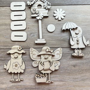 May include: Wooden craft kit featuring a birdhouse, a flower, a bird with an umbrella, a bird with a watering can, a bird with a hat, and a set of five blank wooden signs.