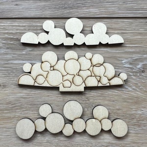 May include: Three wooden decorative pieces with a light wood grain finish. Each piece features a series of connected circles in varying sizes. The pieces are arranged on a wooden surface, showcasing their unique shapes and designs.