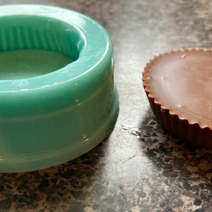 May include: A teal silicone mold for making peanut butter cups, next to a finished peanut butter cup.