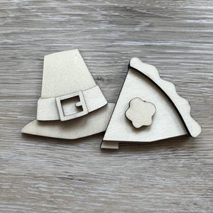 May include: Two wooden craft shapes, one a pilgrim hat with a buckle and the other a pie crust with a flower design.