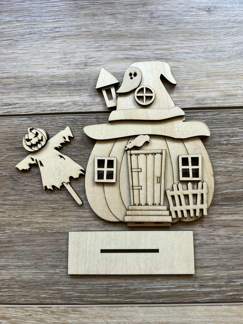 May include: A wooden Halloween decoration featuring a pumpkin-shaped house with a witch hat roof, windows, and a door. A scarecrow and a base are included. The decoration is made of unfinished wood.