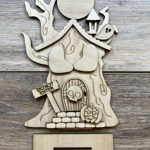 May include: A wooden Halloween-themed decoration featuring a tree with a house, a full moon, and a ghost. The house has a skull door and a pumpkin. The sign reads "DO NOT ENTER". Includes a stand.