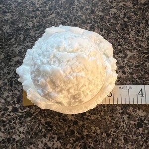 K&ouml;nnte beinhalten: Ein wei&szlig;er, runder, strukturierter Eisportionierer mit einem Durchmesser von etwa 10 cm ist auf einer braunen, gefleckten Oberfl&auml;che zu sehen. Der Portionierer besteht aus einem Material, das Styropor &auml;hnelt.