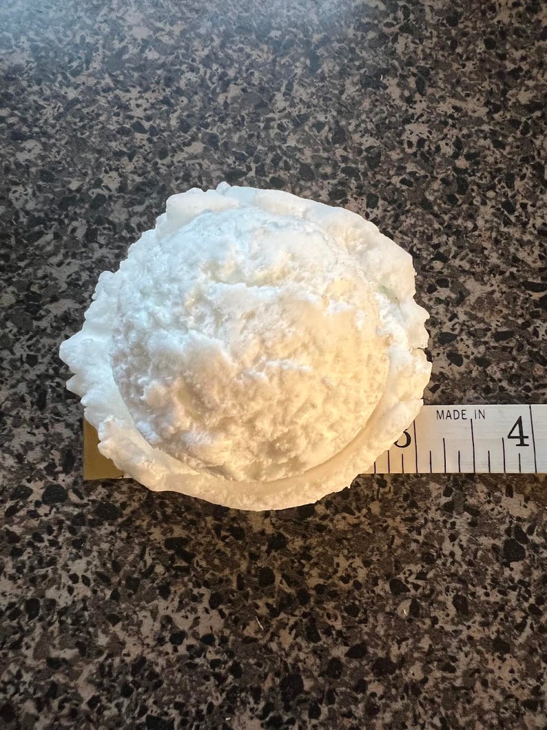 K&ouml;nnte beinhalten: Ein wei&szlig;er, runder, strukturierter Eisportionierer mit einem Durchmesser von etwa 10 cm ist auf einer braunen, gefleckten Oberfl&auml;che zu sehen. Der Portionierer besteht aus einem Material, das Styropor &auml;hnelt.