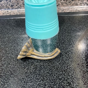 May include: A gold-colored metal decorative hook with a floral design. The hook is lying on a black surface.