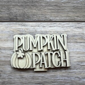 May include: Wooden sign with the words "Pumpkin Patch" in a decorative font. A small pumpkin with a leaf is to the left of the words.
