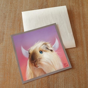 May include: Square greeting card featuring a whimsical illustration of a fluffy, light-colored creature with blue eyes and white horns, set against a pink and purple gradient background. The card is framed in gray and accompanied by a blank envelope.