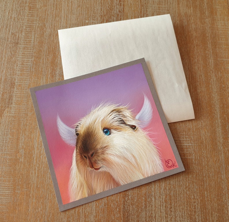 May include: Square greeting card featuring a whimsical illustration of a fluffy, light-colored creature with blue eyes and white horns, set against a pink and purple gradient background. The card is framed in gray and accompanied by a blank envelope.