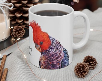 Puede incluir: Taza de cerámica blanca con una ilustración colorida de un loro de cabeza roja. El loro tiene la cabeza roja, el cuerpo gris y los ojos negros. La taza tiene un asa negra y está llena de café.