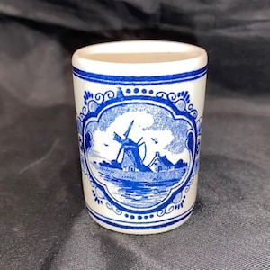 May include: A white ceramic mug with a blue and white windmill scene. The mug has a blue and white border with a decorative design.