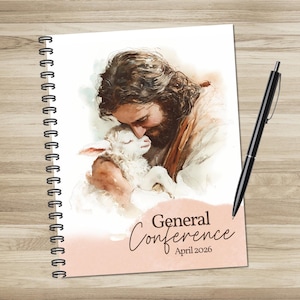 Puede incluir: Cuaderno con espiral con una ilustración en acuarela de una persona abrazando a un cordero. La portada tiene las palabras "General Conference April 2026". Un bolígrafo negro descansa en el lado derecho del cuaderno.