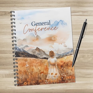 Peut inclure: Cahier à spirales avec une illustration à l'aquarelle. La couverture présente le texte "General Conference" au-dessus d'un paysage avec une femme dans un champ. Un stylo noir repose sur le côté droit du cahier.