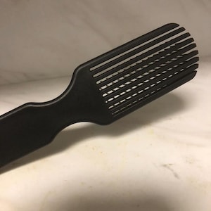 May include: A black plastic hair brush with a wide, rectangular head and a grid pattern of bristles. The brush is designed to detangle and smooth hair.