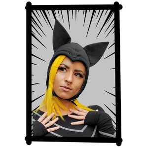 May include: A black hooded hat with pointed ears, resembling a bat, worn by a person with yellow hair. The person is wearing a black long-sleeved shirt with gray accents. The background is gray with white radial lines.