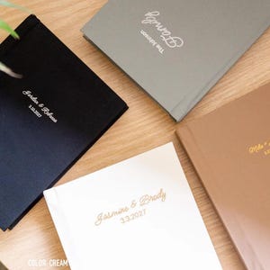 May include: Four rectangular photo albums in black, sage, mocha, and cream colors. Each album features personalized text in a script font on the front cover, including names and dates such as Jordan & Rebecca 2.10.2027, The Johnson Family, Jasmine & Brody 3.3.2027, and Mike & Jennifer 5.13.2027.
