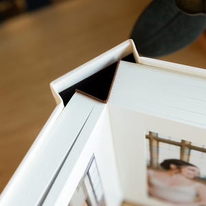 May include: A white photo album with a brown leather spine and a white frame around a photo of a couple. The album is closed and the photo is visible through the frame.