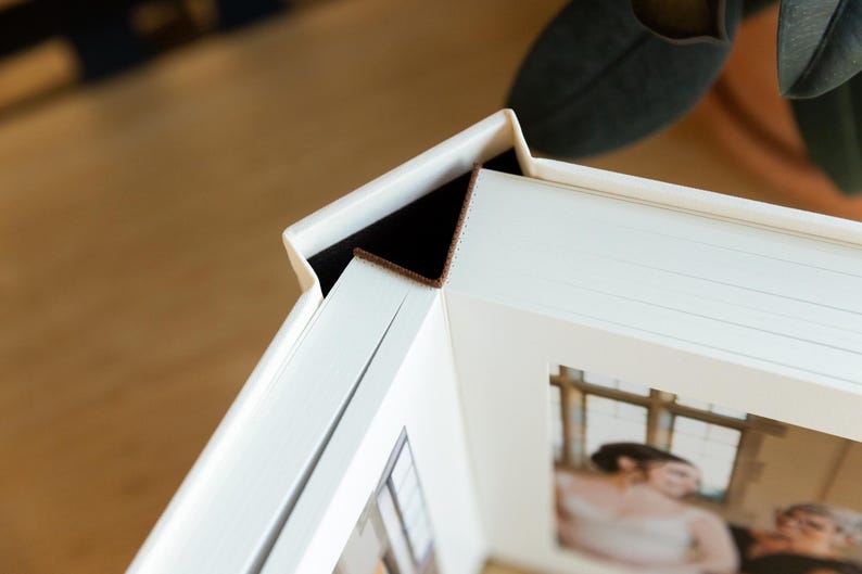 May include: A white photo album with a brown leather spine and a white frame around a photo of a couple. The album is closed and the photo is visible through the frame.