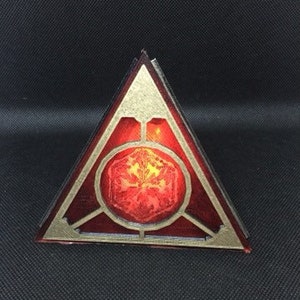 Peut inclure: Un prisme triangulaire rouge avec un cadre doré et un motif hexagonal rouge lumineux au centre.