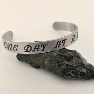 May include: A silver bracelet with the inscription "One Day At A Time" engraved on it.