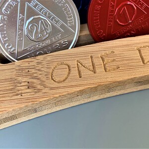 May include: A wooden box with the words "ONE DAY" engraved on the front. The box has slots for holding round tokens, and one slot is filled with a silver token with the words "24 HOURS" and "RECOVERY" on it.