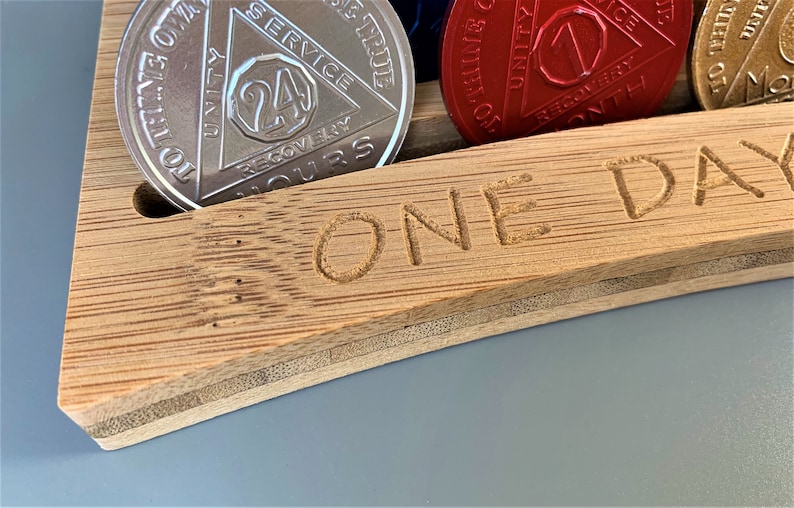 May include: A wooden box with the words "ONE DAY" engraved on the front. The box has slots for holding round tokens, and one slot is filled with a silver token with the words "24 HOURS" and "RECOVERY" on it.