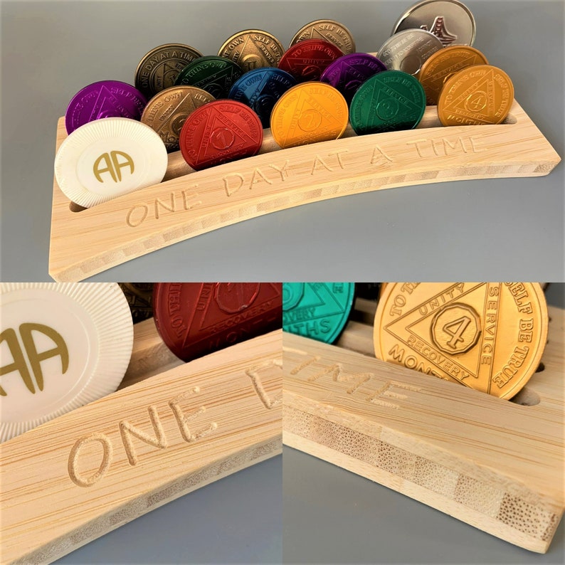 May include: A wooden coin holder with the inscription "One Day At A Time" and a row of gold, silver, and colorful medallions. The medallions have various numbers and inscriptions, including "Unity, Service, Self Be True, Recovery, Months".