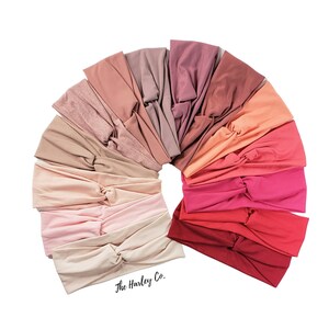 May include: A set of 18 knotted headbands in a variety of shades of pink, red, and orange. The headbands are arranged in a semi-circle, with the darkest shades at the top and the lightest shades at the bottom. The text "The Harley Co." is visible at the bottom of the image.