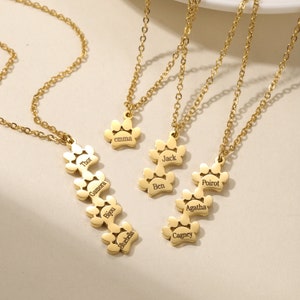 May include: Three gold necklaces with paw print charms. Each charm has a different name engraved on it: Thor, Gamora, Bijou, Bluebella, Emma, Jack, Ben, Poirot, Agatha, and Cagney.