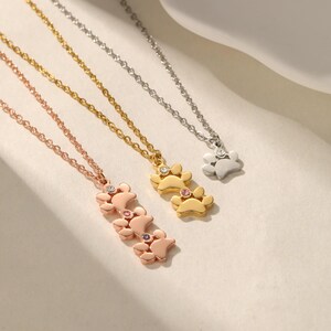 May include: Three necklaces with paw print pendants. One is rose gold with pink and clear gems, one is gold with clear and pink gems, and one is silver with a clear gem.