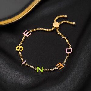 May include: A gold chain bracelet with colourful enamel letters spelling out the word "FRIEND" with a sliding clasp.