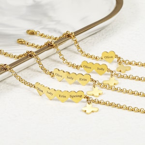Puede incluir: Cuatro pulseras de cadena dorada con dijes en forma de corazón. Cada dije en forma de corazón tiene un nombre grabado: Olive, Judy, Erin y Spring. Las pulseras también tienen un dije de mariposa.