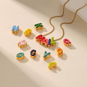 Può includere: Una collana color oro con la parola "MAIL" scritta con lettere smaltate colorate. Ulteriori singole lettere in vari colori sono sparse intorno alla collana. Le lettere sono blu, gialle, verdi, rosa e arancioni.