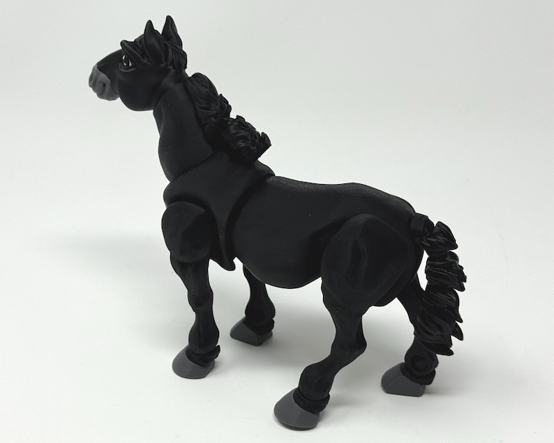 May include: A black horse figurine with a detailed mane and tail. The horse is posed in a standing position, with its head turned slightly to the left. The hooves are gray. The figurine is made of a matte material.
