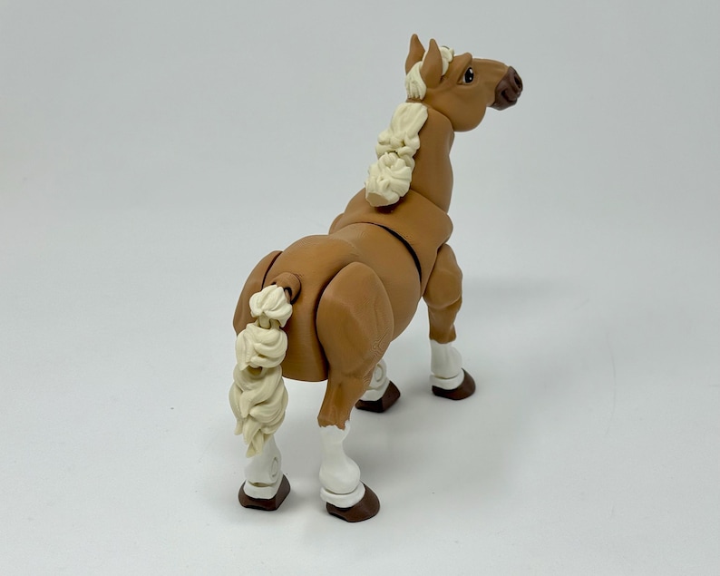 May include: A brown toy horse with a cream-colored mane and tail. The horse has white markings on its legs and hooves. The toy is posed with its head turned to the side, and its tail is curled.