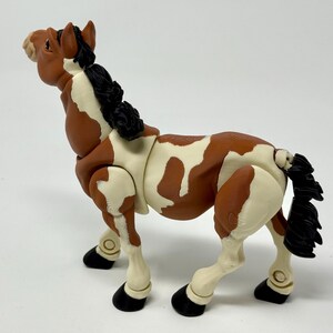 May include: A brown and white toy horse with a black mane and tail. The horse has black hooves and is posed in a standing position. The toy horse is made of plastic and has a detailed design.